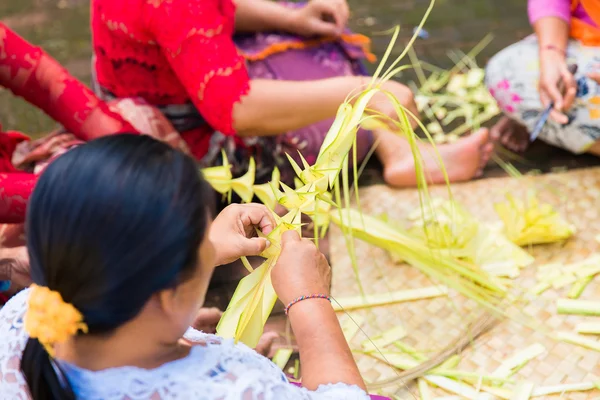 Bali, Indonesia, May 3, 2015. Balinese women make decorations of palm leaves for the feast at the local temple in Bali, Indonesia. Offering flowers and other gifts is very popular tradition on Bali.