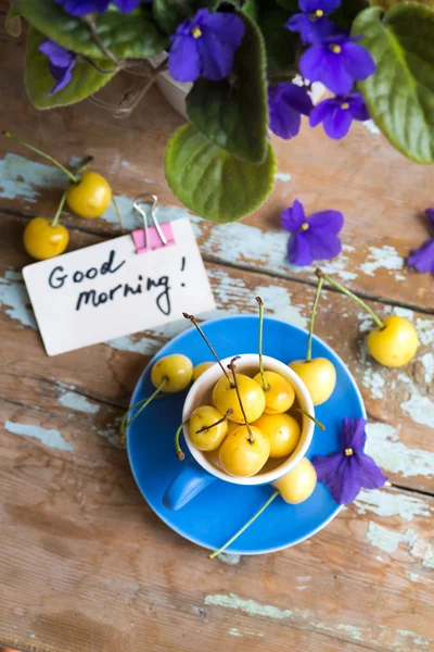 Blue tea cup full with yellow cherries with violets in a pot
