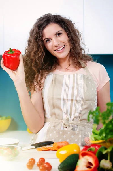 Young woman holding a red pepper and cooking healthy food