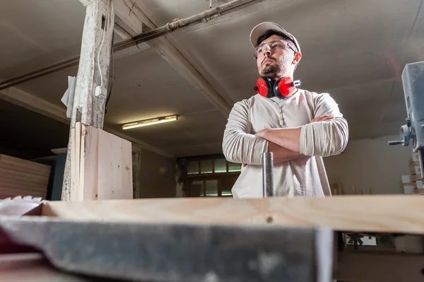 Carpenter working with Industrial tool in wood factory wearing safety glasses and hearing protection.