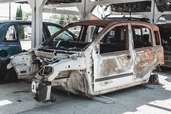 Rusted torched car in a dismantling yard.