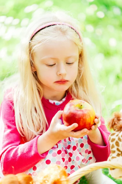 Pretty little blonde girl holding a bitten apple, an looking sad