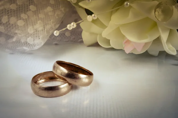 Two wedding rings lie on a light horizontal surface against a bo