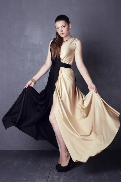 Young brunette lady in black ang golden dress posing on grey background