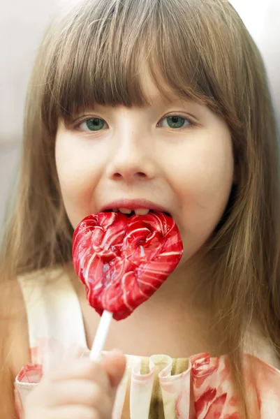 Portrait of a little girl with lollipop caramel heart on a stick