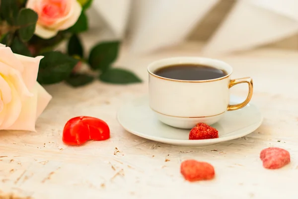 Cup of coffee, sugar hearts and a bouquet of cream roses