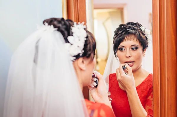 Preparation of bride. girl with lipstick. Woman looking at the mirror and she is putting lip gloss