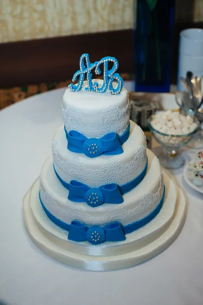 Wedding cake in white and blue combination, adorned with flowers, ribbons.