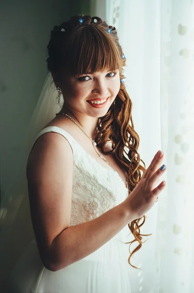 Young beautiful bride waits for groom near the window. Beautiful  young woman standing beside a large window waiting