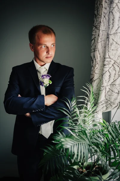Portrait of handsome groom in classical interior. Man against window  background dress cufflinks.