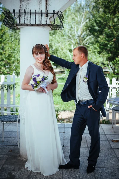 Wedding couple kissing in green summer park. bride and groom kissing, standing together outdoors, hugging among green trees. Bride holding wedding bouquet of flowers