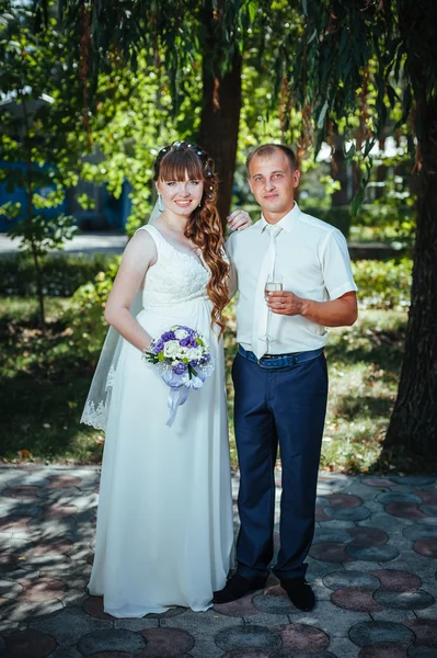 Wedding couple kissing in green summer park. bride and groom kissing, standing together outdoors, hugging among green trees. Bride holding wedding bouquet of flowers