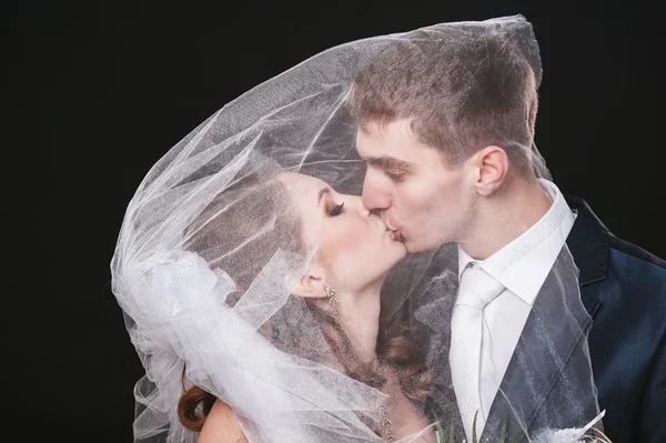 Bride And Groom Kissing Under Veil Holding Flower Bouquet In Hand. black background