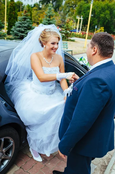 Happy groom helping his bride out of the wedding car.