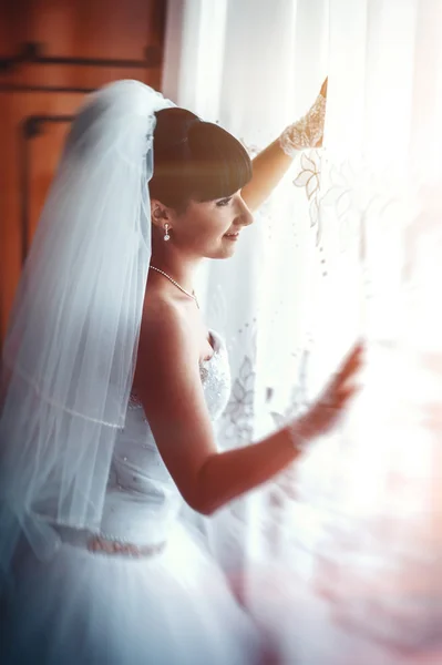 Beautiful bride getting ready in white wedding dress with hairstyle and bright makeup. Happy sexy girl waiting for groom. Romantic lady in bridal dress have final preparation for wedding.
