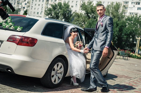 Happy groom helping his bride out of the wedding car