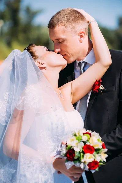 A wedding by the sea. Honeymoon. The bride and groom hugging on the shore of Lake. groom and bride hugging on a green lake. Groom and Bride in a park. wedding dress. Bridal wedding bouquet of flowers.