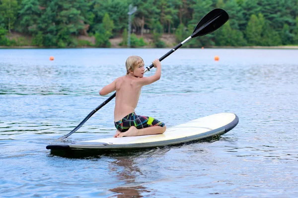 Teenage boy camping and enjoying stand up paddle on the lake