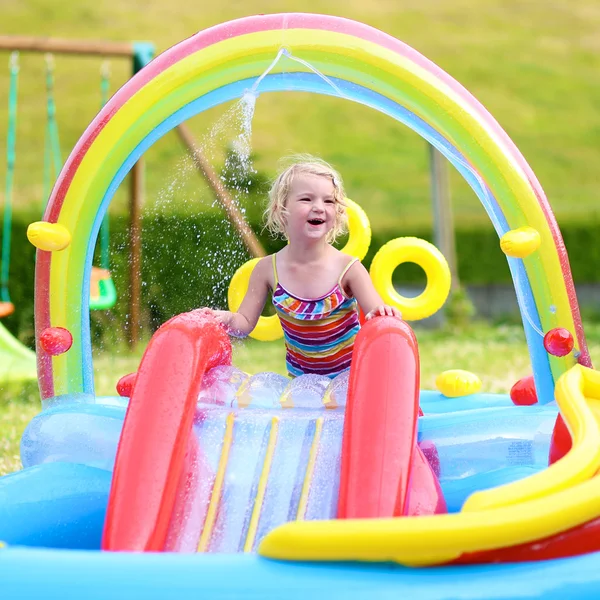 Happy little girl splashing in inflatable swimming pool in the garden