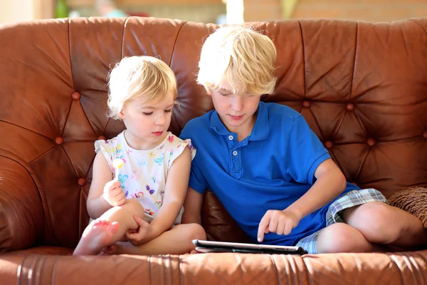 Brother and sister playing with tablet pc on sofa