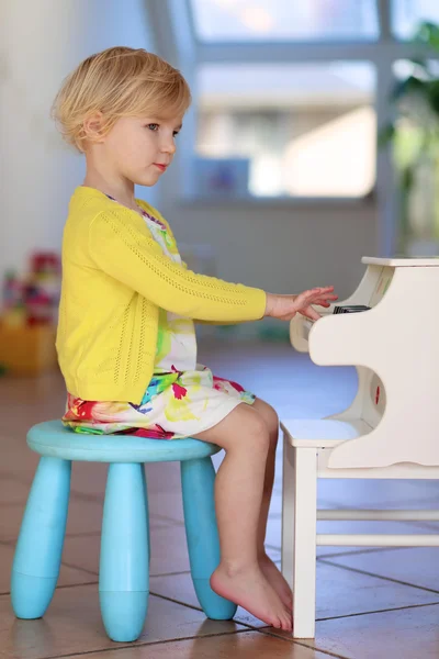 Little girl playing piano toy at home