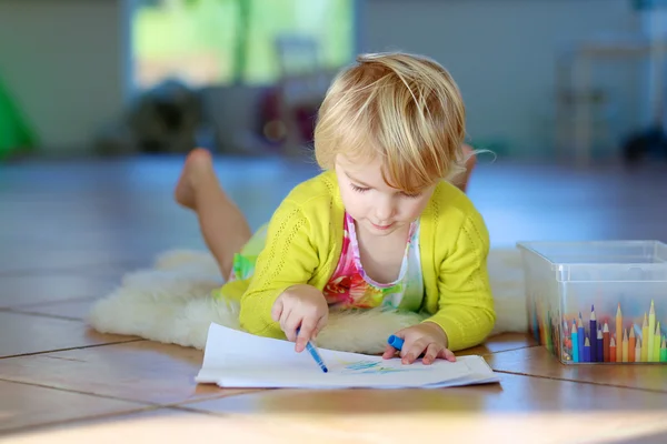 Small girl drawing on paper lying on the floor