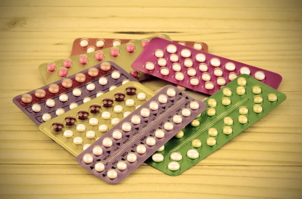 Colorful oral contraceptive pill strips on pine wood table.