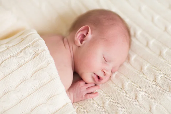 Tiny newborn baby sleeping on a soft knitted blanket