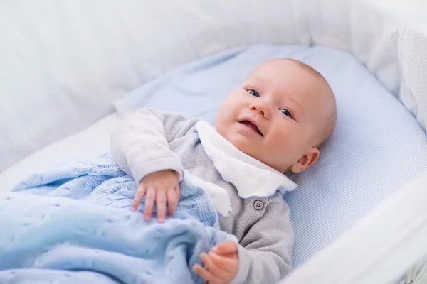 Baby boy in a crib under knitted blanket