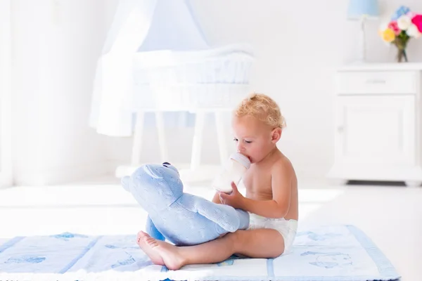 Baby boy with milk bottle in sunny nursery