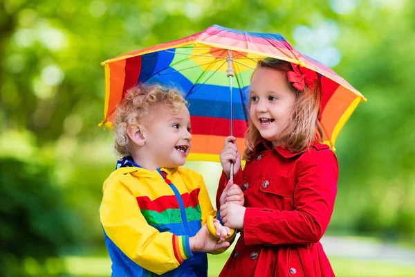Kids playing in the rain under colorful umbrella