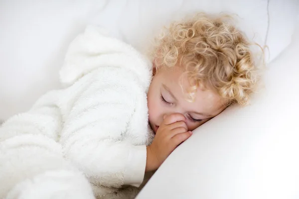 Cute blond curly little boy sleeping on white couch