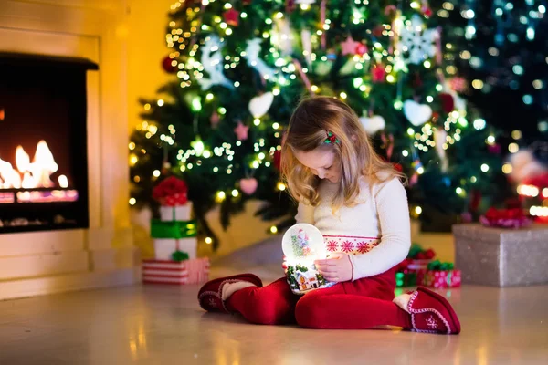 Little girl holding snow globe under Christmas tree