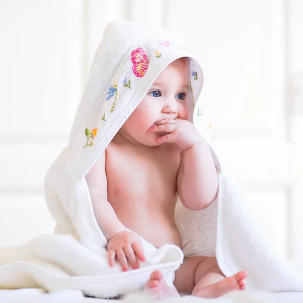 Adorable baby girl sitting under a hooded towel after bath