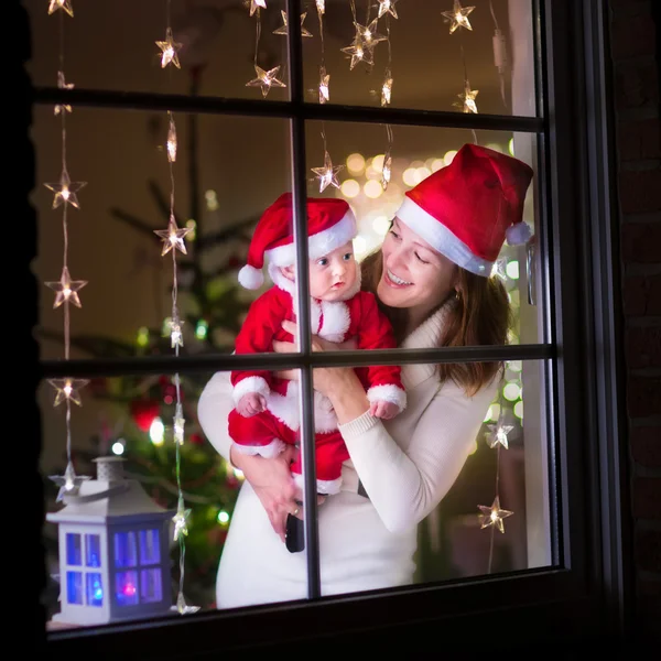 Mother and baby dressed as Santa at a window on Christmas