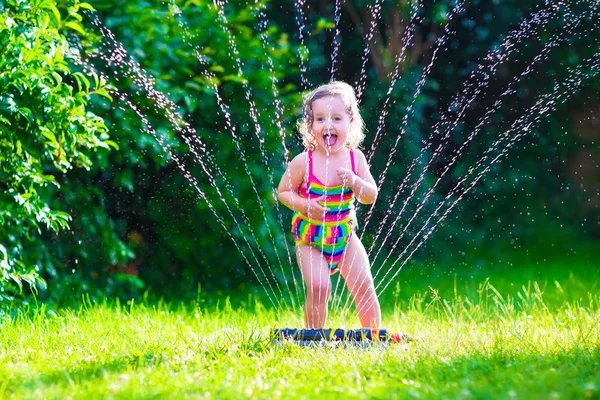 Little girl playing with garden water sprinkler