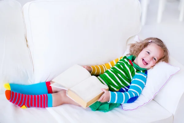 Little girl reading a book on a white couch