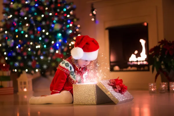 Little girl opening Christmas presents next to a fire place