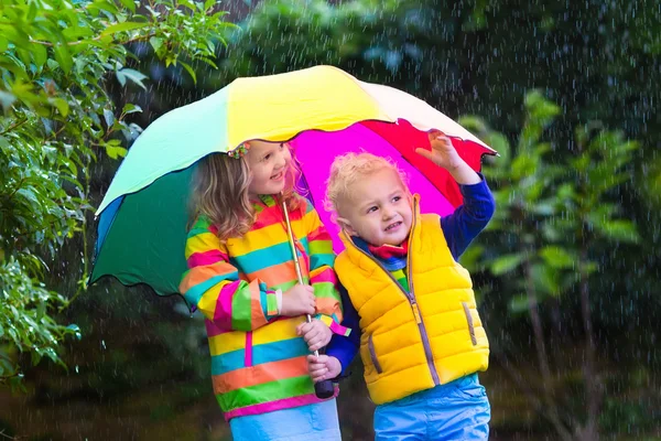 Kids playing in the rain under colorful umbrella