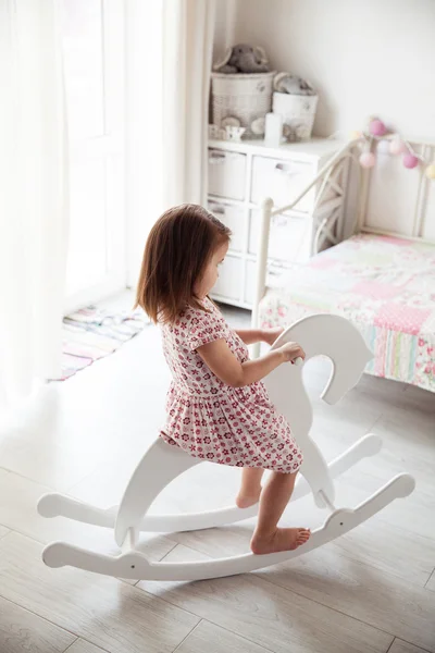 Beautiful smiling baby girl on a toy wooden horse. Brunette, toy, game