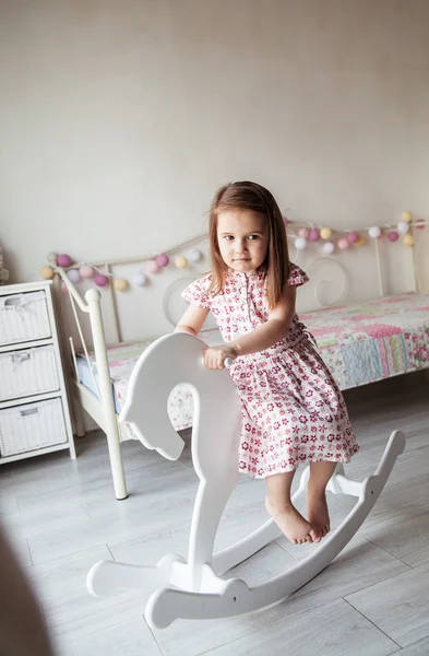 Beautiful smiling baby girl on a toy wooden horse. Brunette, toy, game