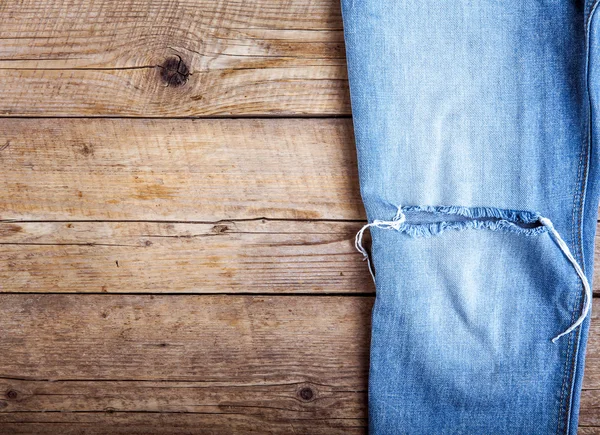 Ripped denim jeans on wooden background. Fashion, clothing, styl
