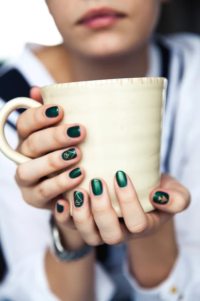 Stylish fashionable girl with a Cup of coffee and a green manicure in jeans. Fashion, care, beauty