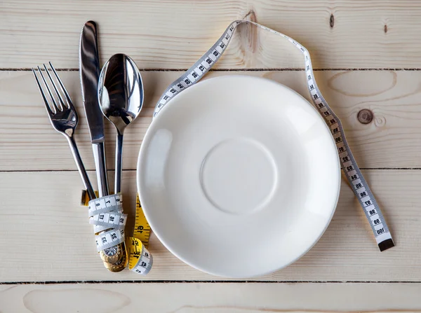 Empty plate with measure tape, knife and fork. Diet food on wooden table
