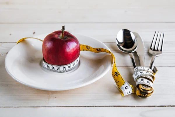 Plate with apple measure tape, knife and fork. Diet food on wooden table