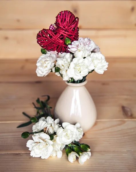 Delicate bouquet of carnations in vintage vase with heart on wooden background. Valentine\'s Day