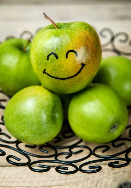 Fruit. fresh green apples in plate on wooden background. with a smile on apple