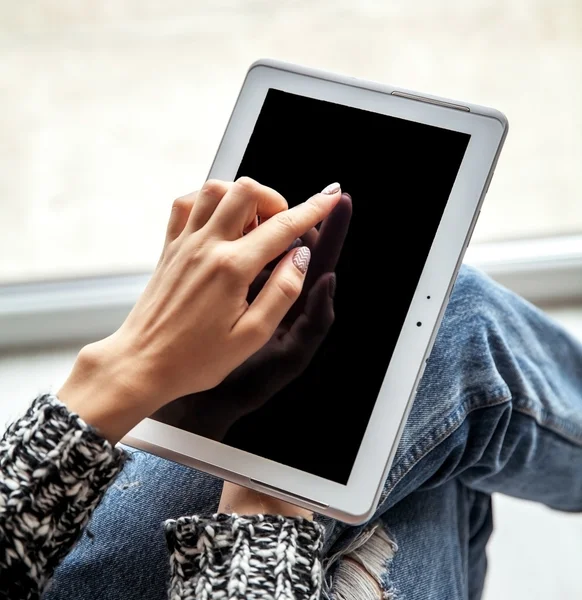 Woman holding and using tablet with empty screen, ripped jeans