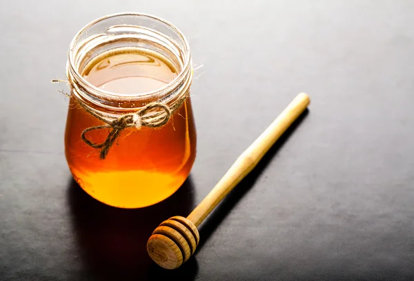 Honey jar and honey dipper against a black background