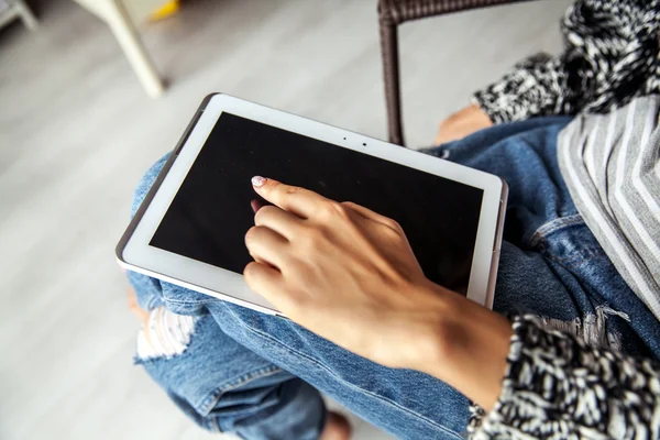 Woman holding and using tablet with empty screen, ripped jeans